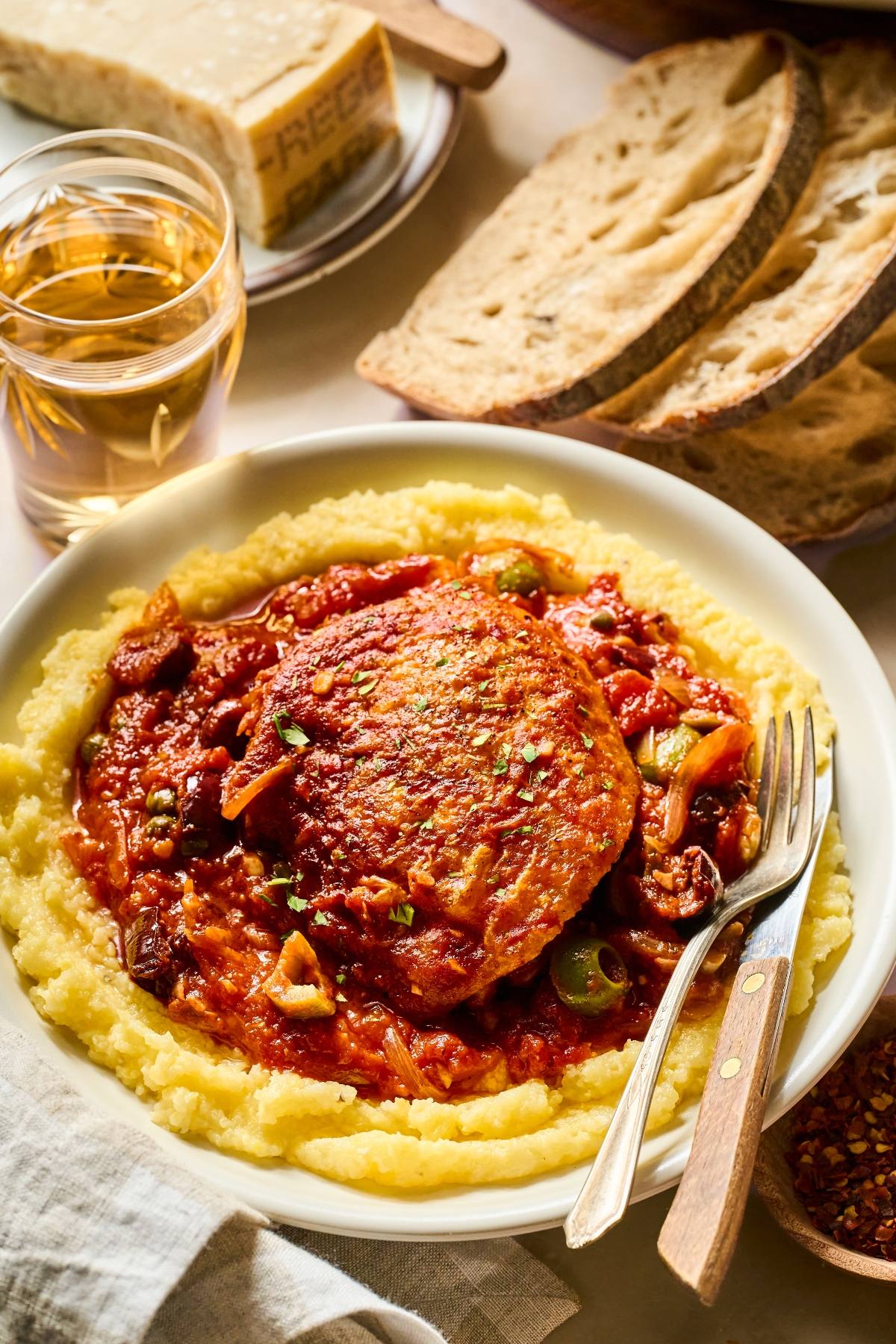 chicken puttanesca in tomato sauce on creamy polenta, served with rustic bread and a glass of white wine.