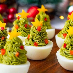 Christmas Tree Deviled Eggs decorated with green topping, red bits, and yellow cheese stars on top make a festive holiday appetizer.