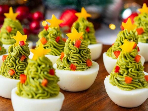 Christmas Tree Deviled Eggs decorated with green topping, red bits, and yellow cheese stars on top make a festive holiday appetizer.