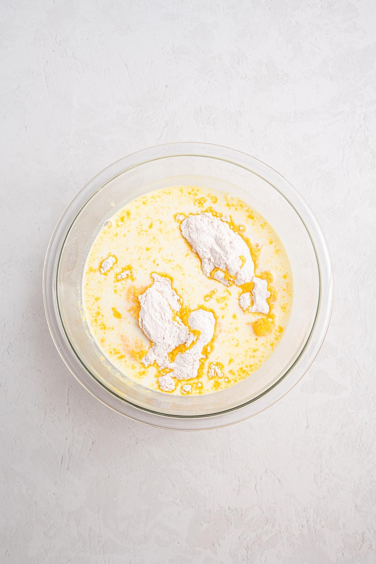 A glass bowl with flour, milk, and melted butter mixture on a light textured surface.