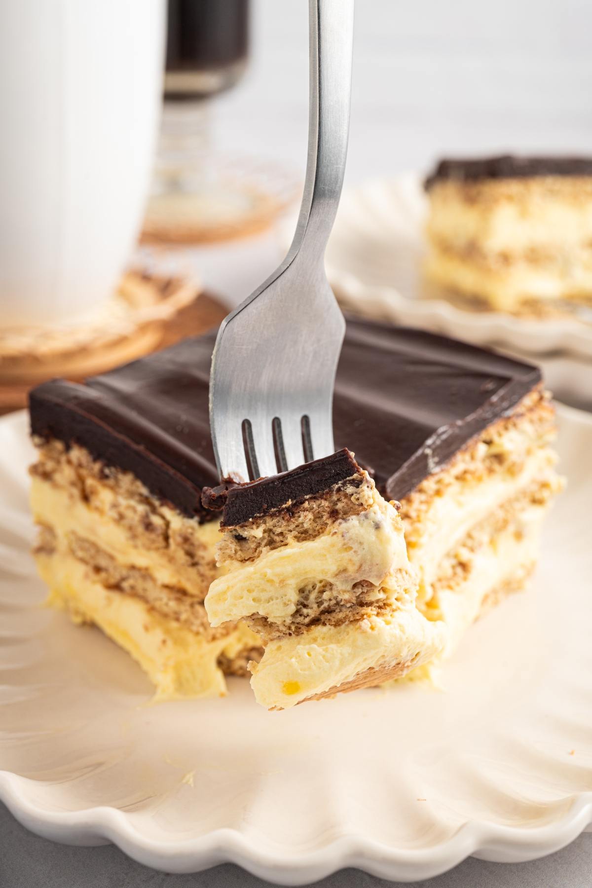 A fork holds a bite of layered chocolate and cream dessert on a white plate.
