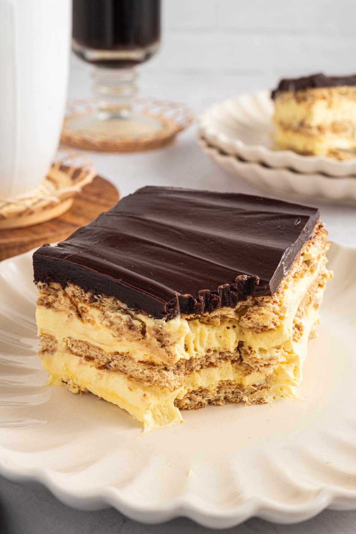 A slice of chocolate-topped layered dessert with cream filling on a white plate.