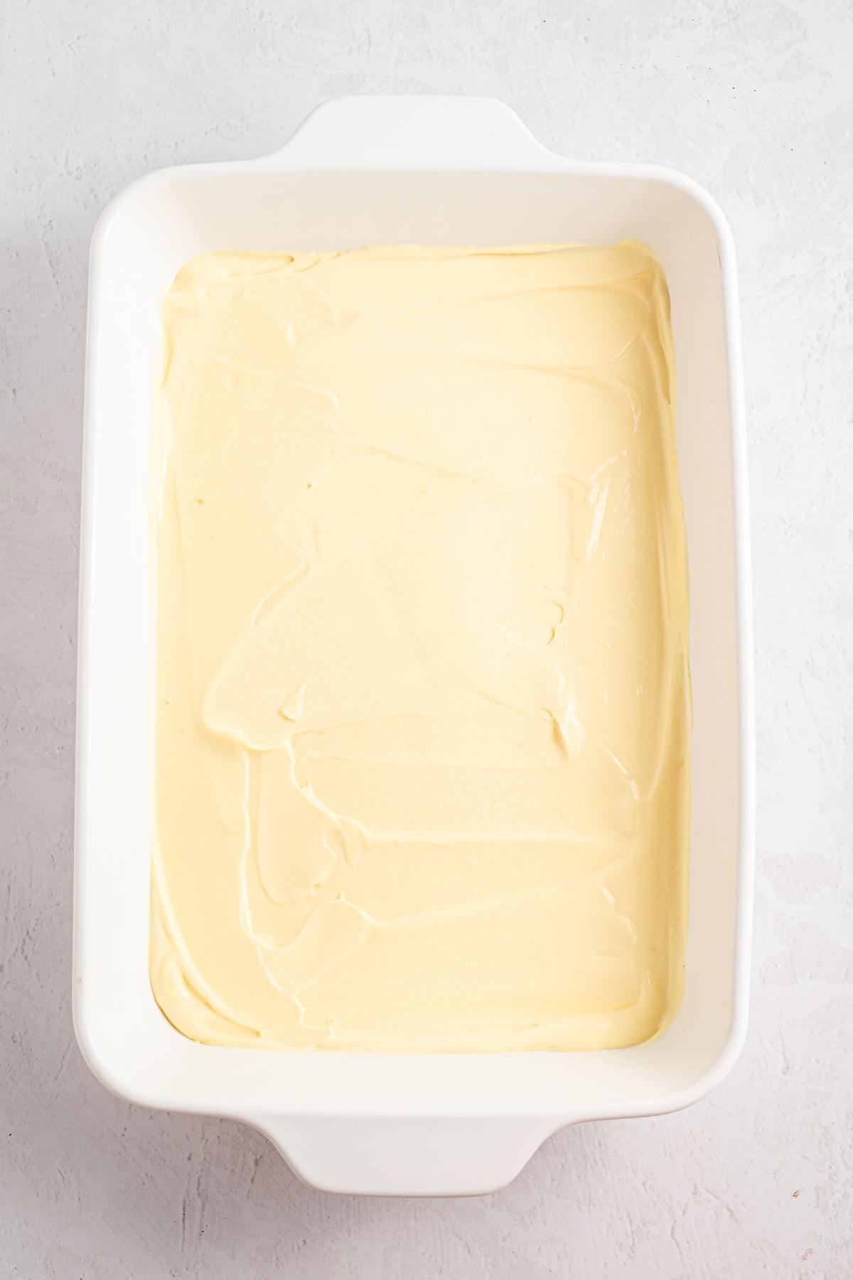 A white baking dish filled with smooth, creamy, light yellow batter on a light gray surface.
