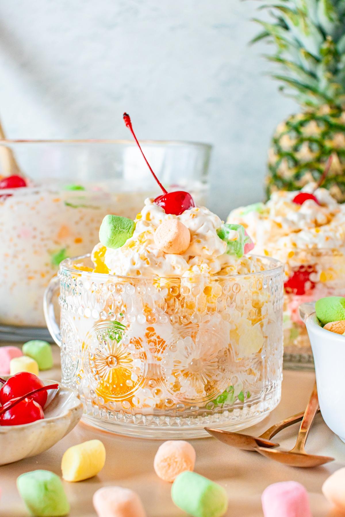 A glass cup filled with creamy frog eye  fruit salad, topped with a cherry and colorful mini marshmallows.