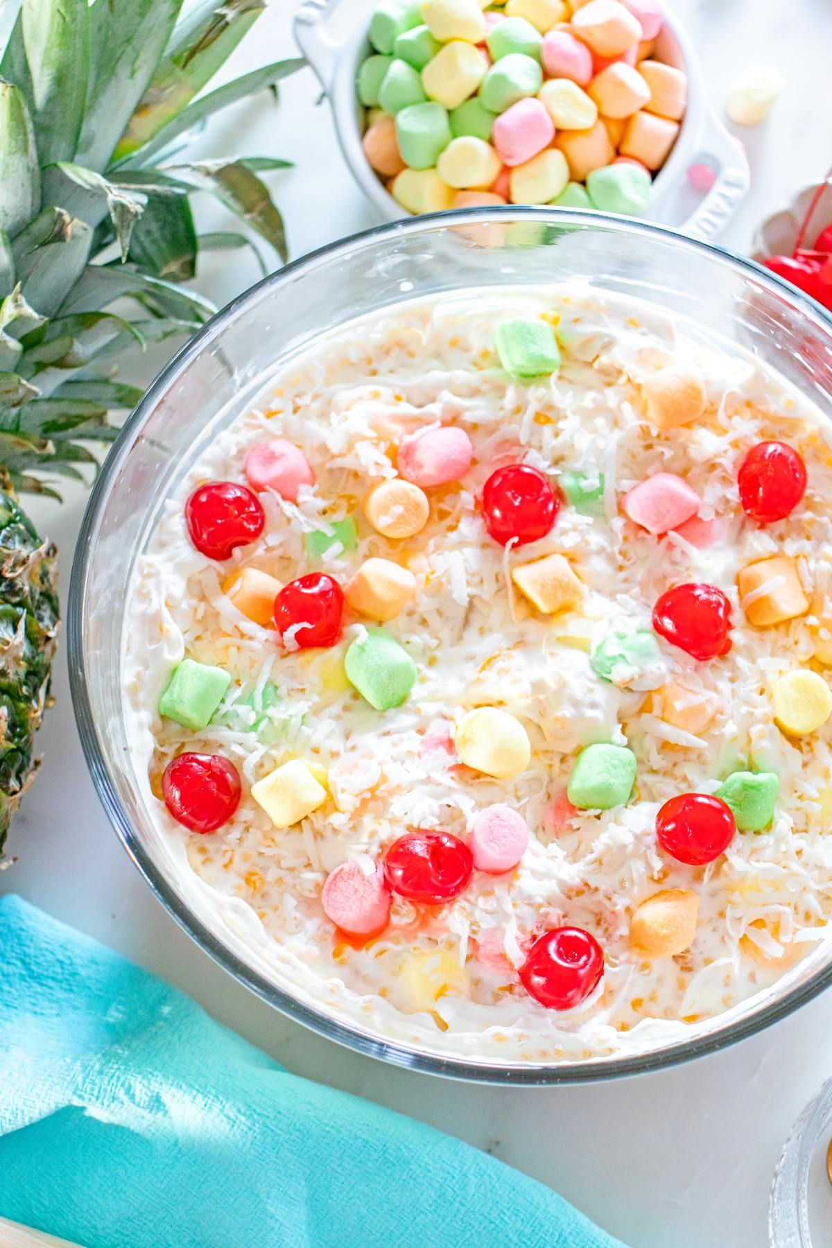 A glass bowl of frog eye  fruit salad topped with colorful marshmallows and maraschino cherries.