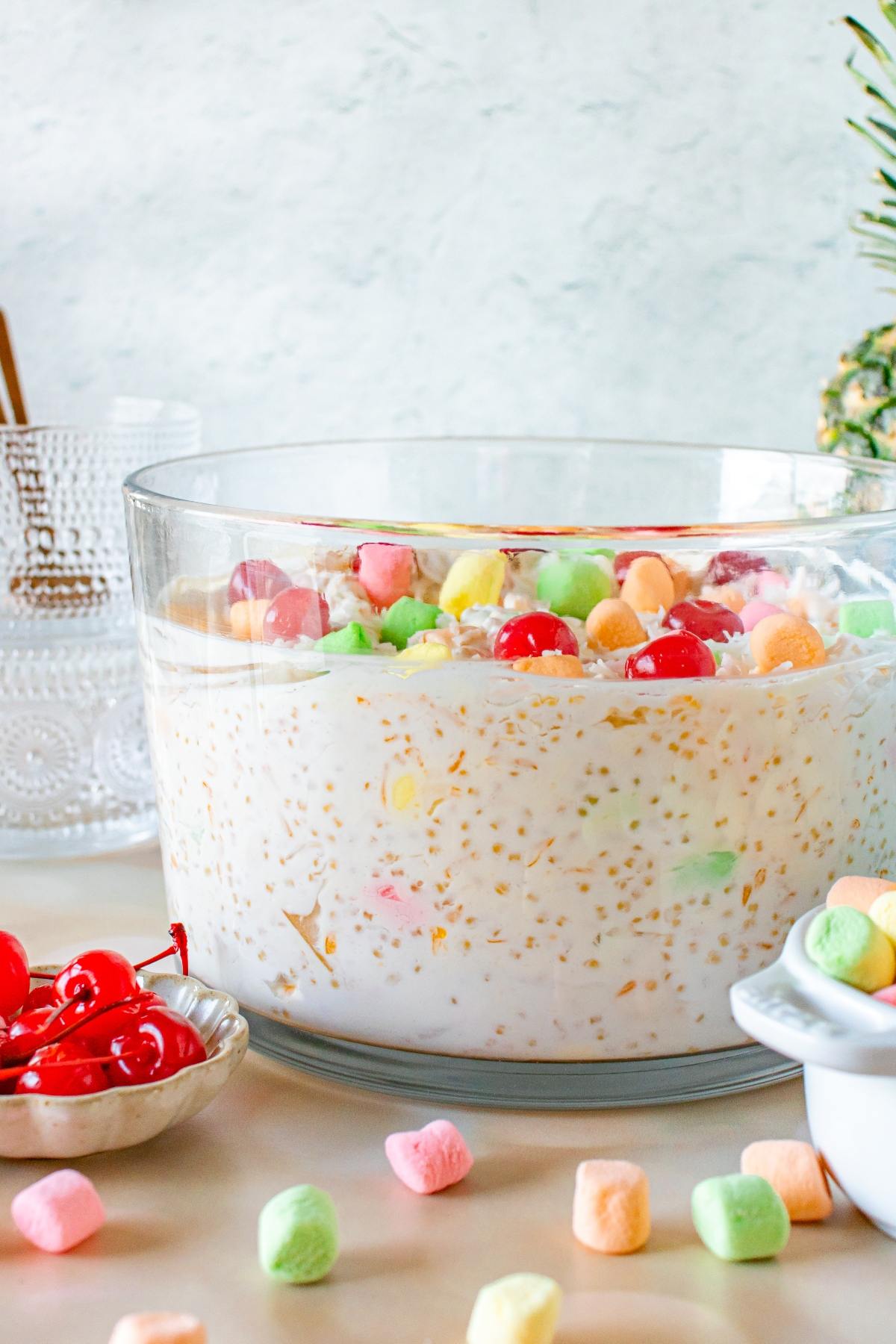 A glass bowl filled with creamy frog eye salad topped with colorful marshmallows and cherries.
