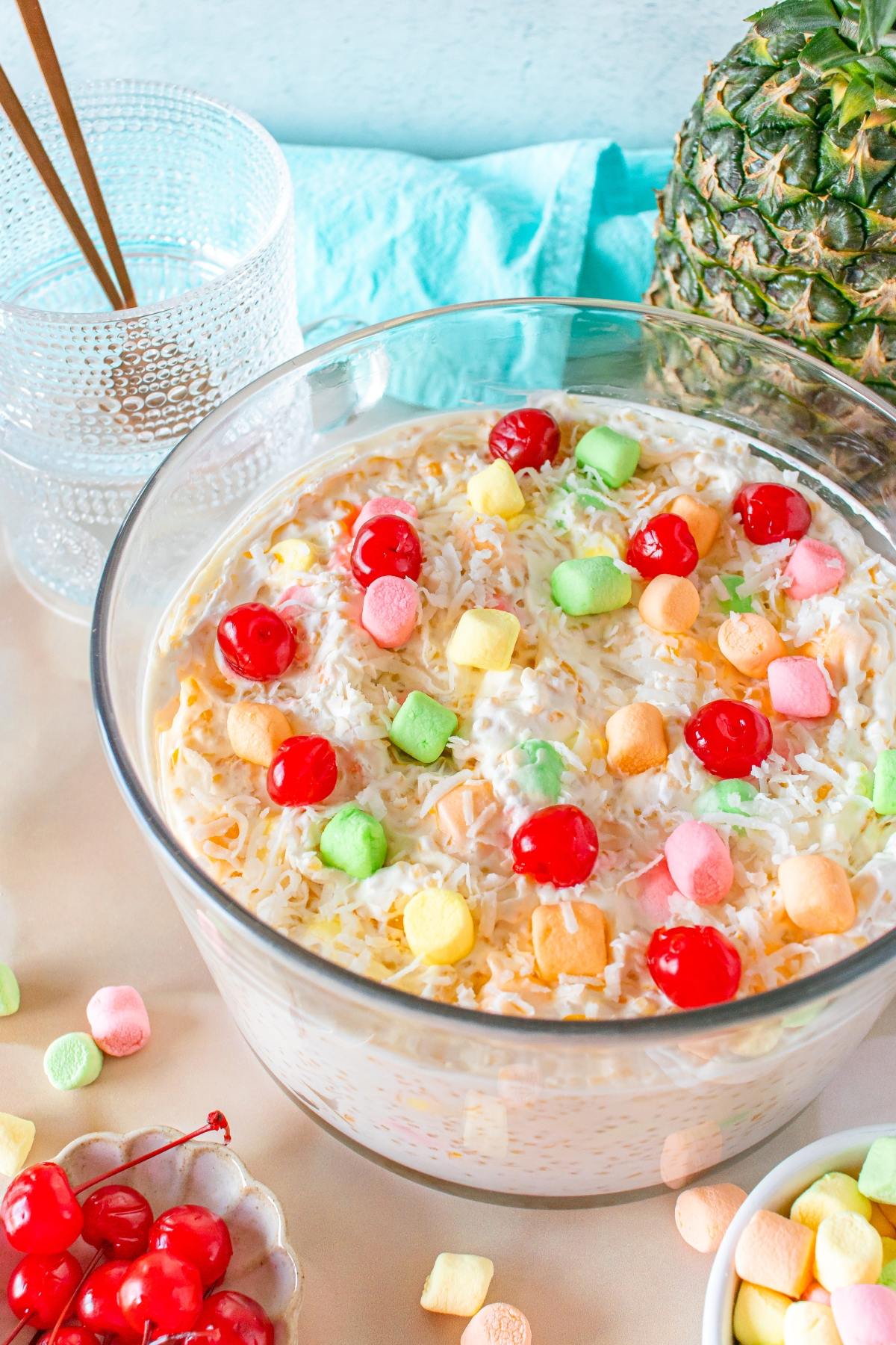 A glass bowl of frog eye salad topped with colorful mini marshmallows and maraschino cherries.