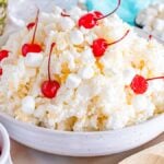 A bowl of glorified rice dessert with whipped cream, marshmallows, pineapple, and maraschino cherries on top.