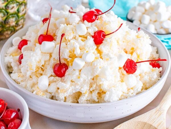 A bowl of glorified rice dessert with whipped cream, marshmallows, pineapple, and maraschino cherries on top.