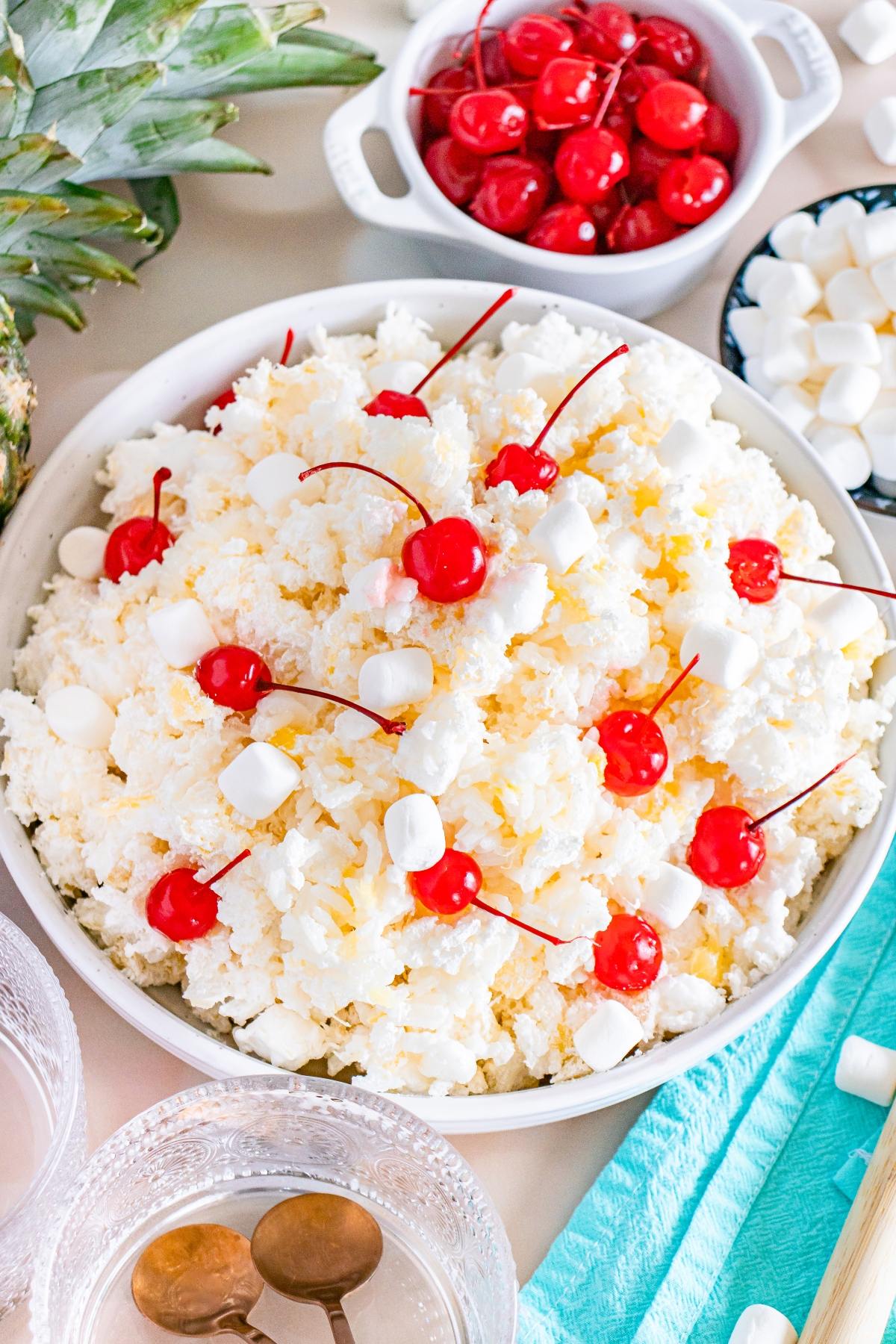 A bowl of glorified rice topped with maraschino cherries and mini marshmallows, surrounded by ingredients.