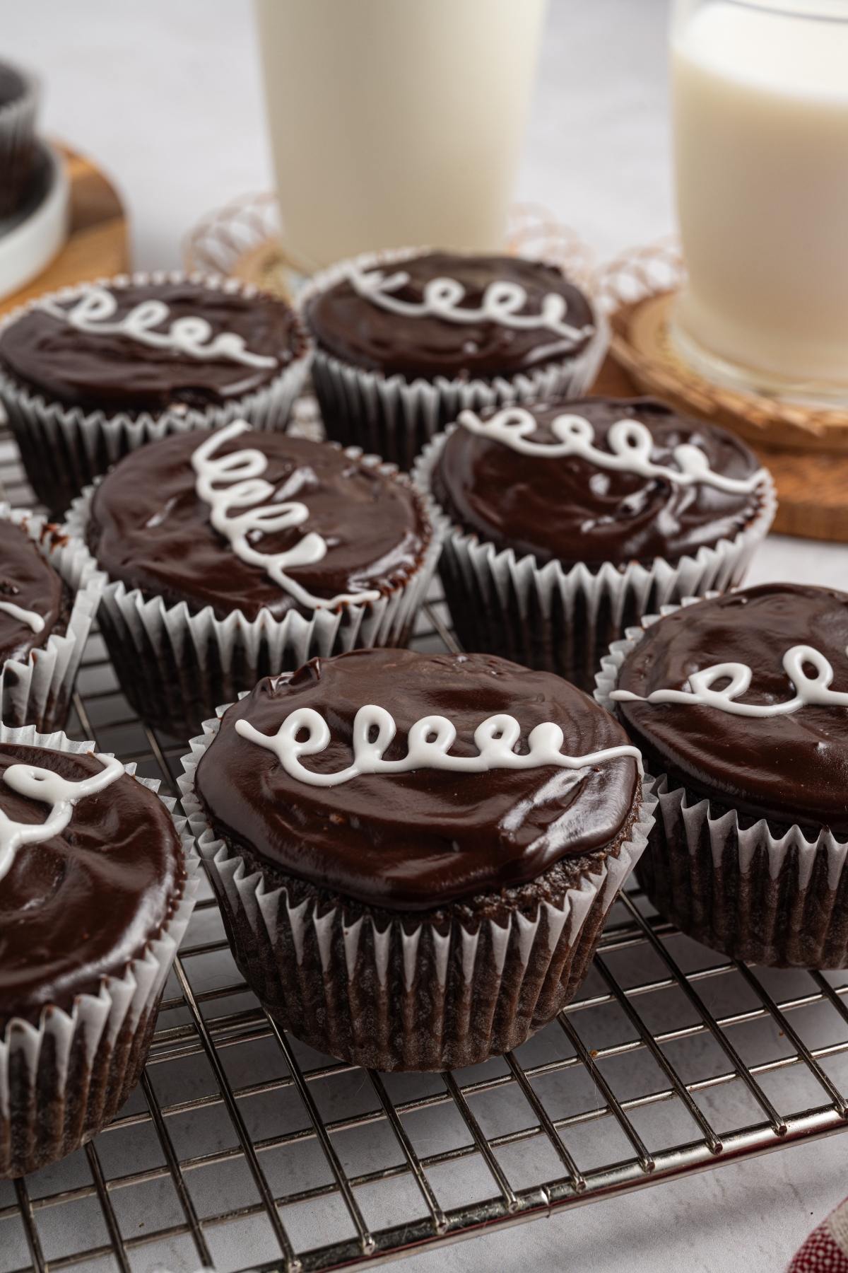 Chocolate homemade hostess cupcakes with glossy icing and a white swirl, on a cooling rack near two glasses of milk.