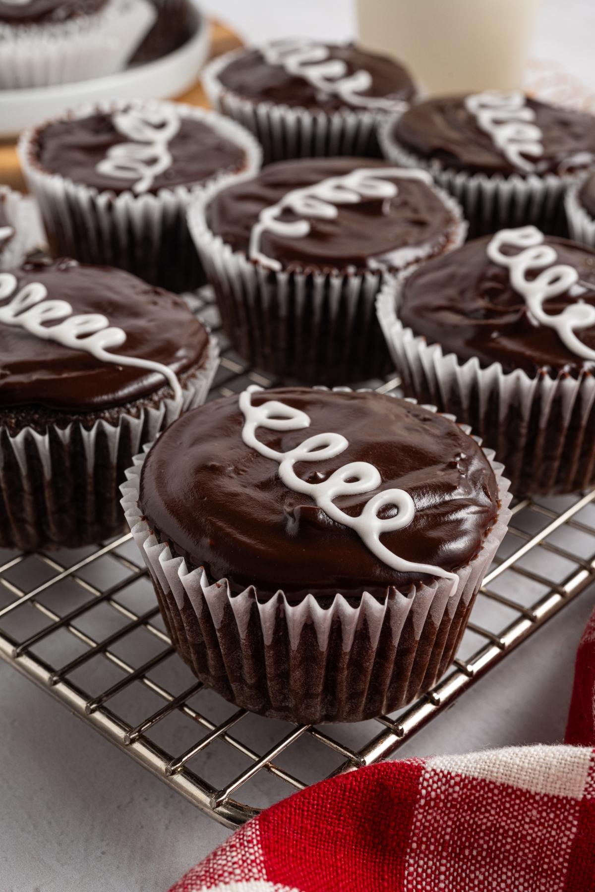 Chocolate homemade hostess cupcakes with glossy icing and white swirl on top, arranged on a cooling rack.
