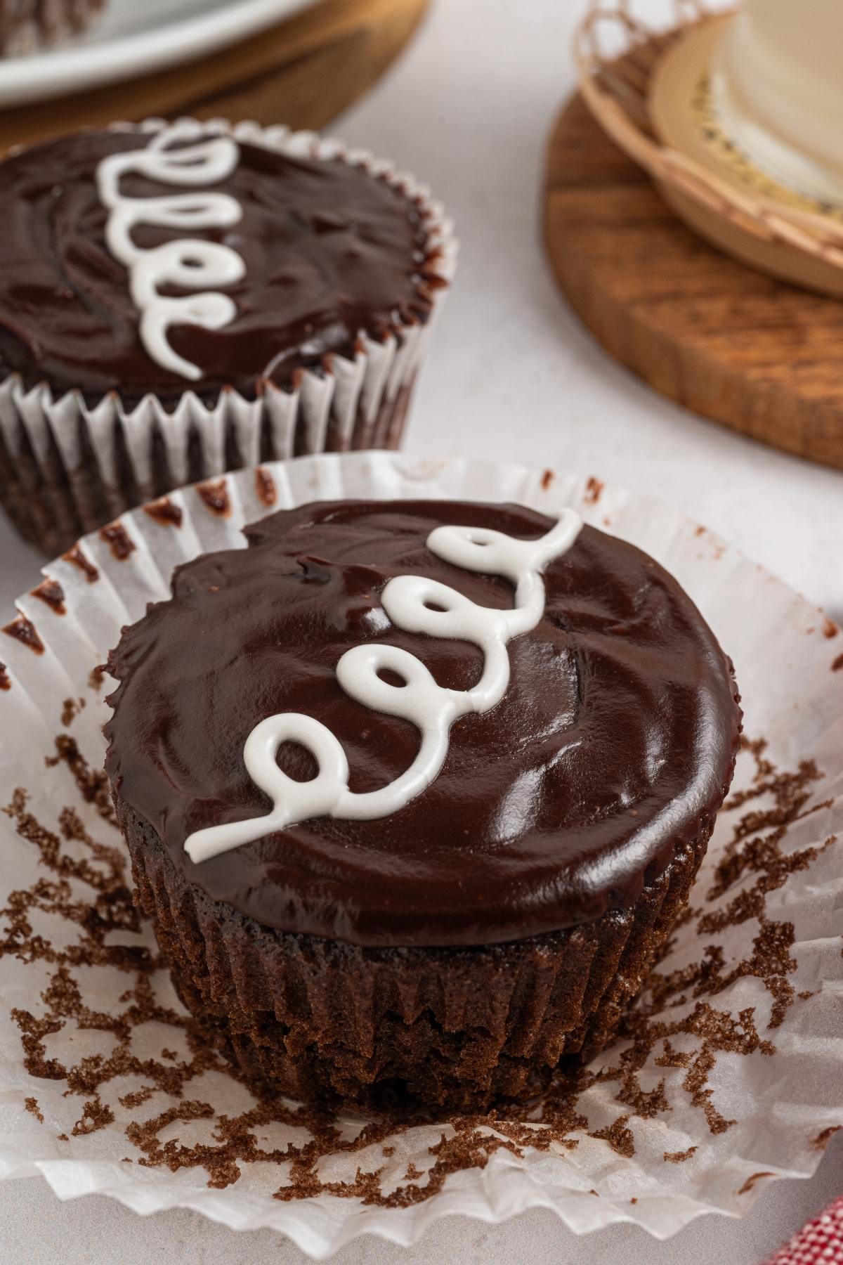 Chocolate homemade hostess cupcake with glossy icing and a white icing swirl on top, partially unwrapped from its paper liner.