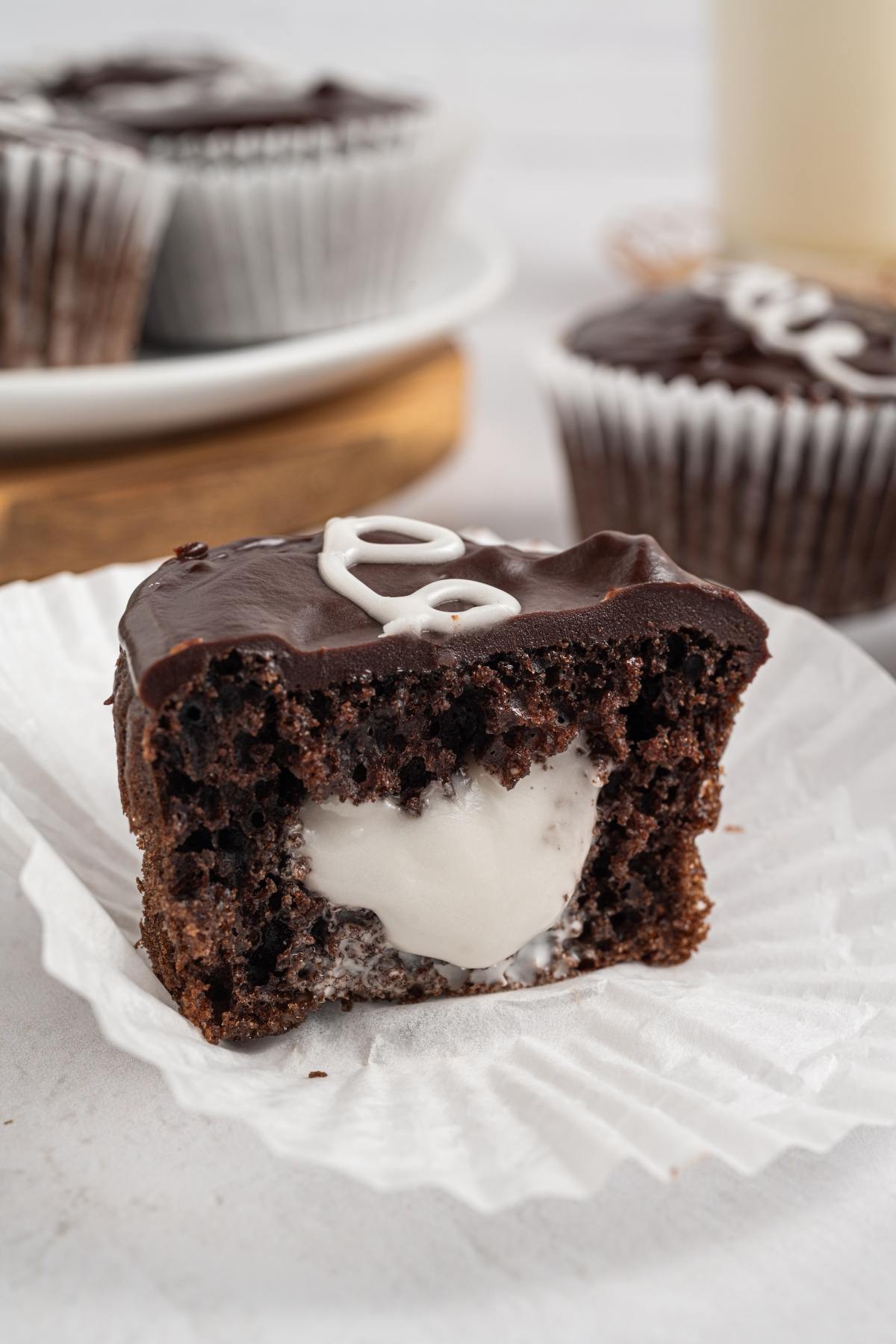 A chocolate homemade hostess cupcake with white cream filling, cut in half, sits on a white paper liner.