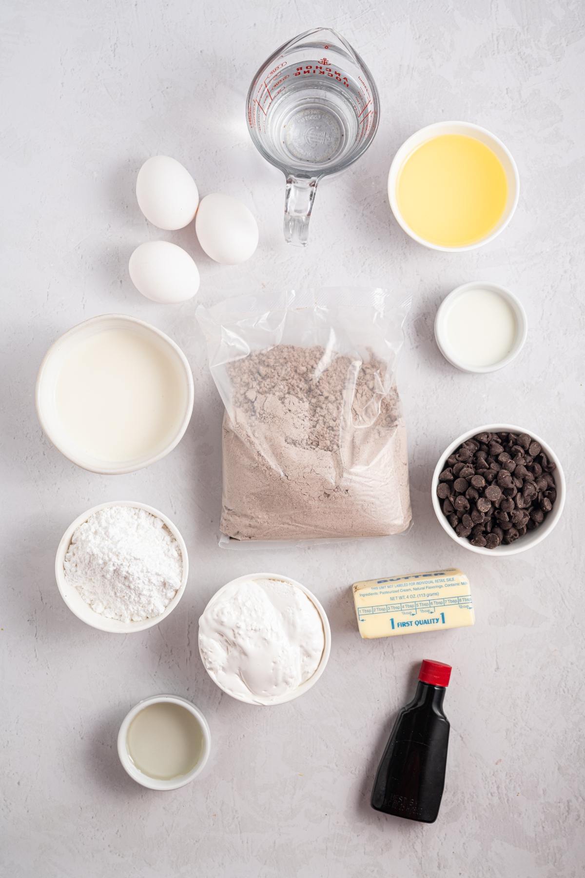 Assorted cake ingredients: eggs, flour, sugar, oil, butter, chocolate chips, cake mix, vanilla, water, and milk.