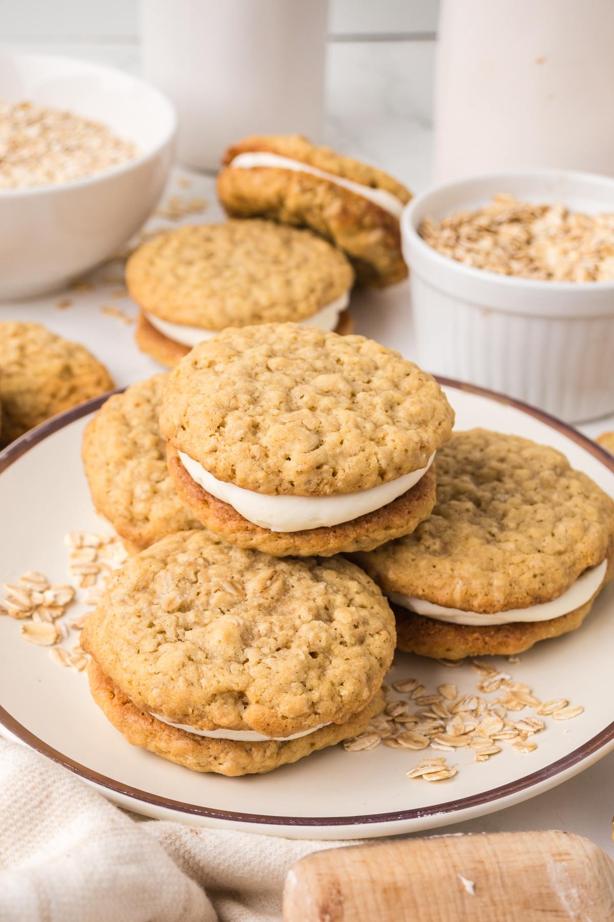 A plate of oatmeal cream pies with oats scattered around and more pies in the background.