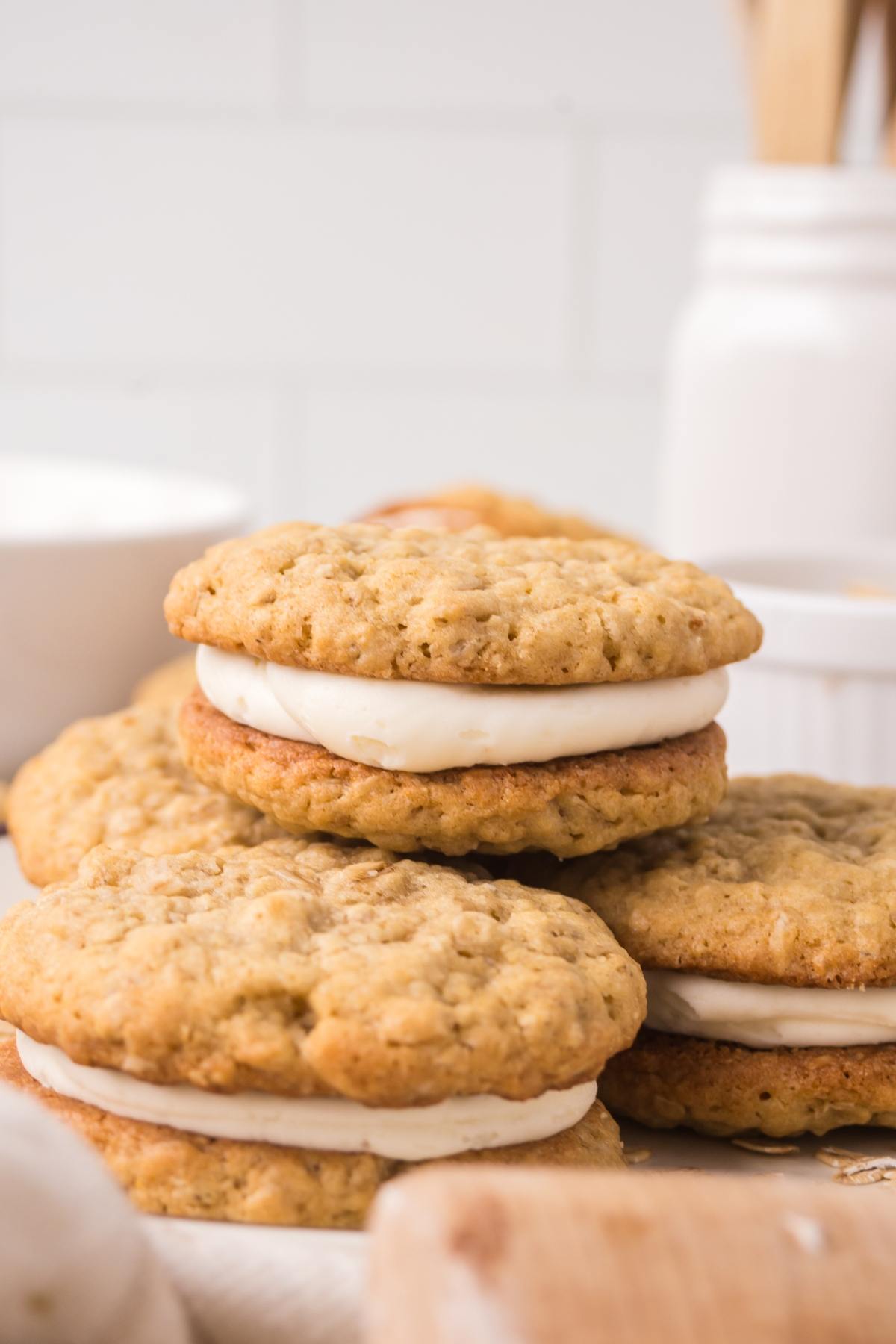 Oatmeal cream pies with white filling stacked on a table in a bright kitchen setting.