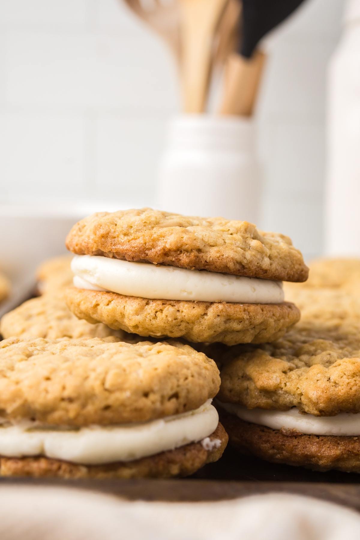 Two oatmeal cream pies stacked with vanilla filling, with more in the background on a kitchen counter.