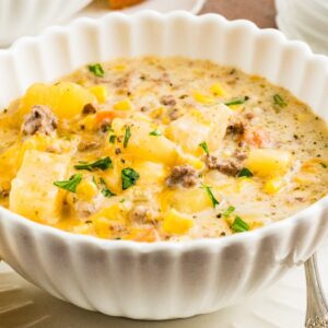 Creamy Slow Cooker Cheeseburger Soup with ground beef, potatoes, and herbs served in a white bowl with a slice of bread on the side.