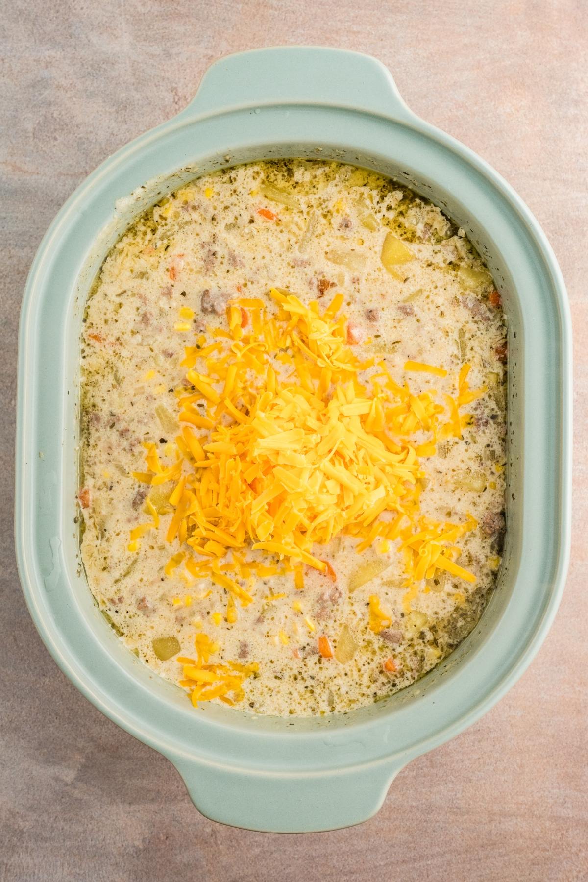 Creamy soup with shredded cheddar cheese on top in a light blue oval casserole dish.