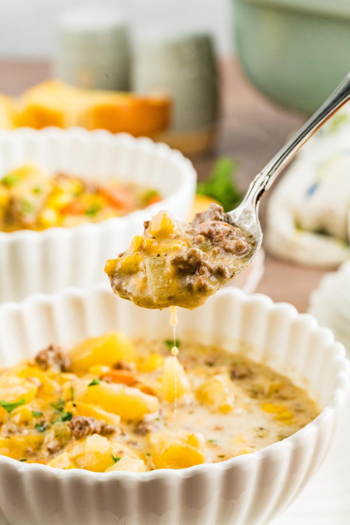 A spoonful of slow cooker cheeseburger creamy soup with ground beef and potatoes held above a white bowl of soup.