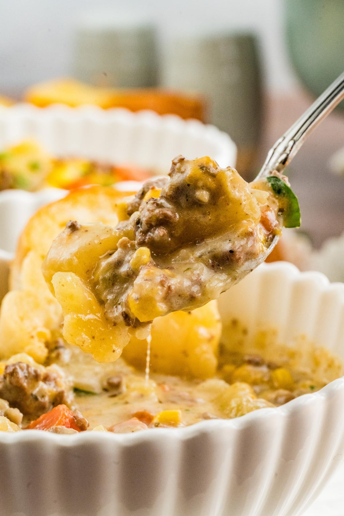 A spoonful of cheesy ground beef and vegetable casserole above a white bowl.