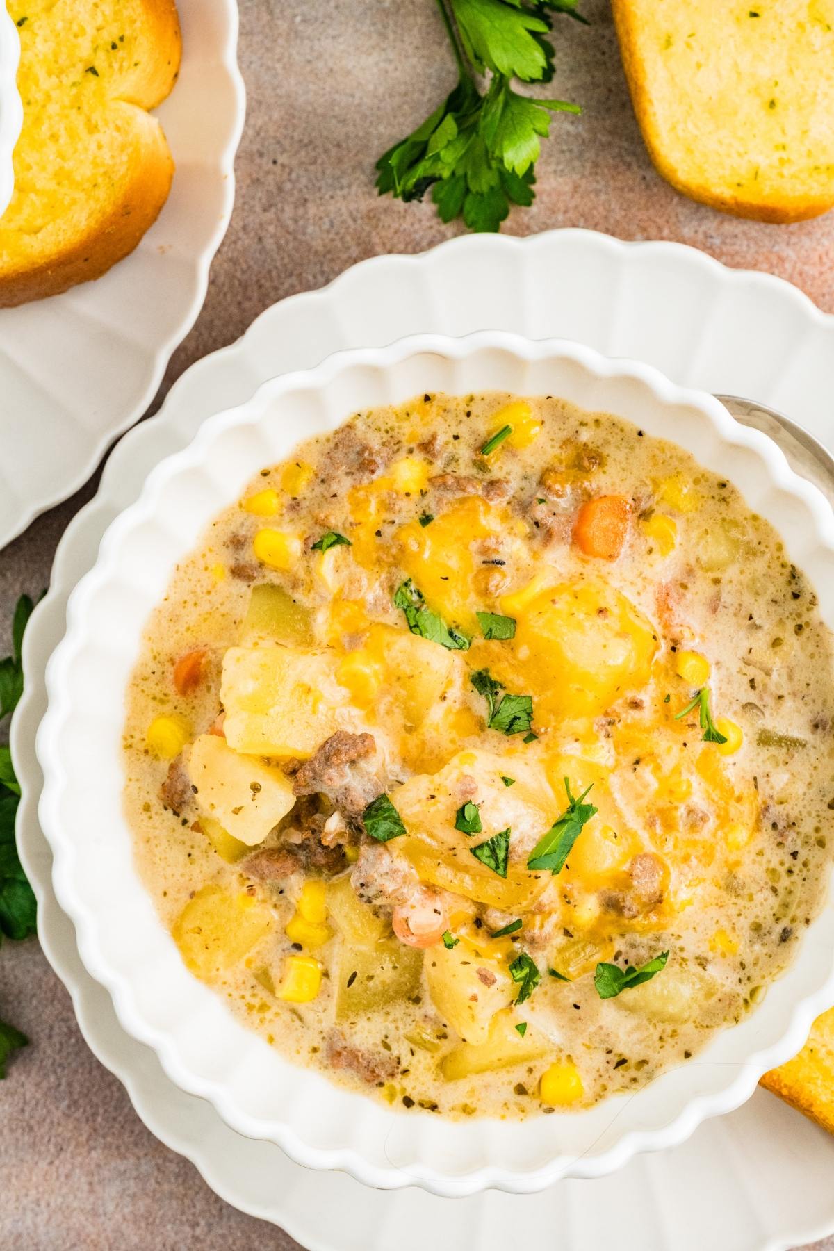 A bowl of slow cooker cheeseburger creamy soup with cheese, potatoes, corn, carrots, and herbs, served with bread on the side.