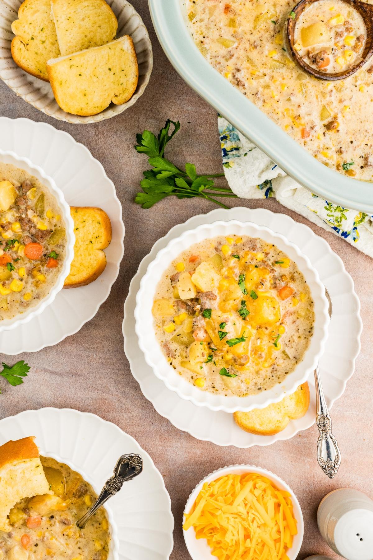 Three bowls of creamy soup with bread, shredded cheese, and parsley on a table, viewed from above.