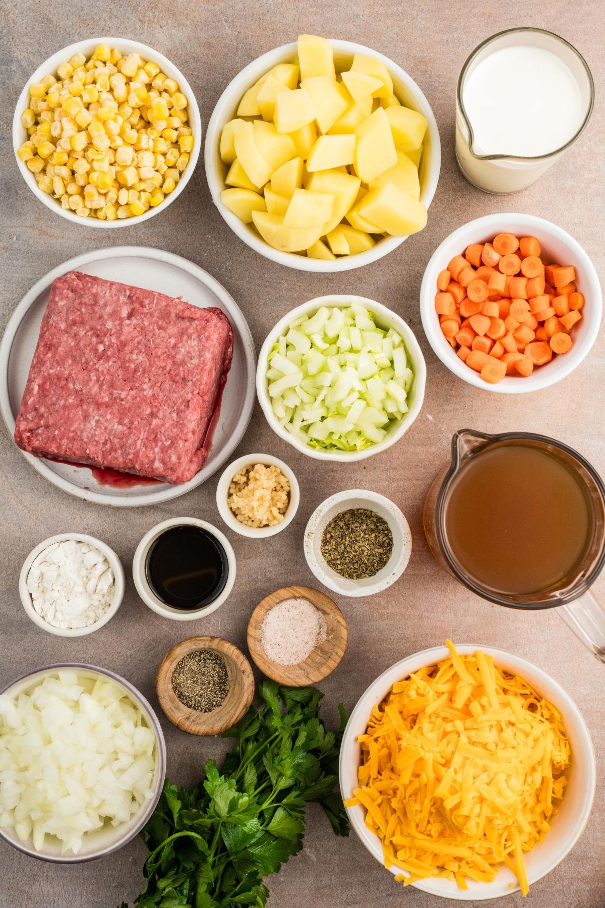 Ingredients for a soup, including ground beef, potatoes, cheese, corn, carrots, celery, onion, broth, and seasonings.