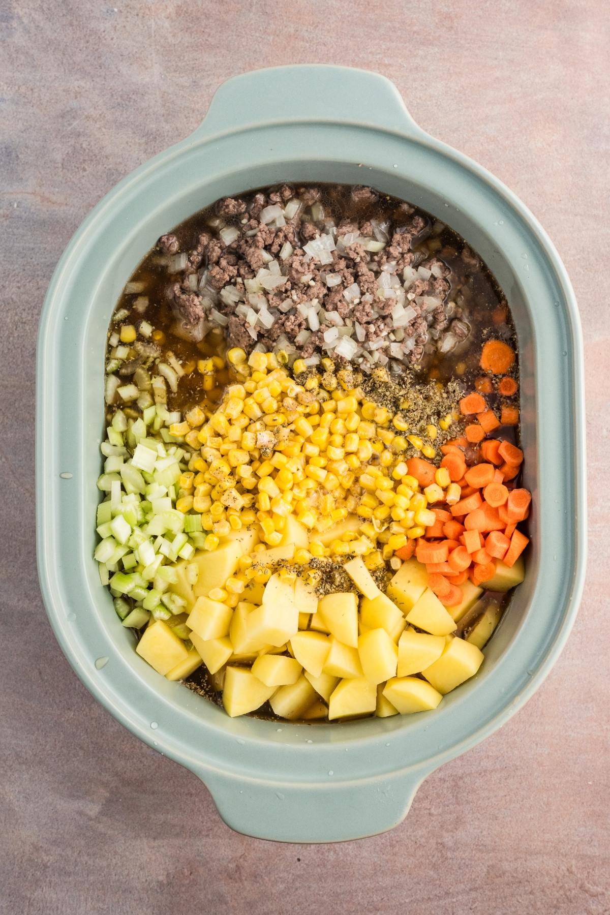Chopped vegetables, ground beef, and corn in a slow cooker, ready to be cooked into a soup or stew.