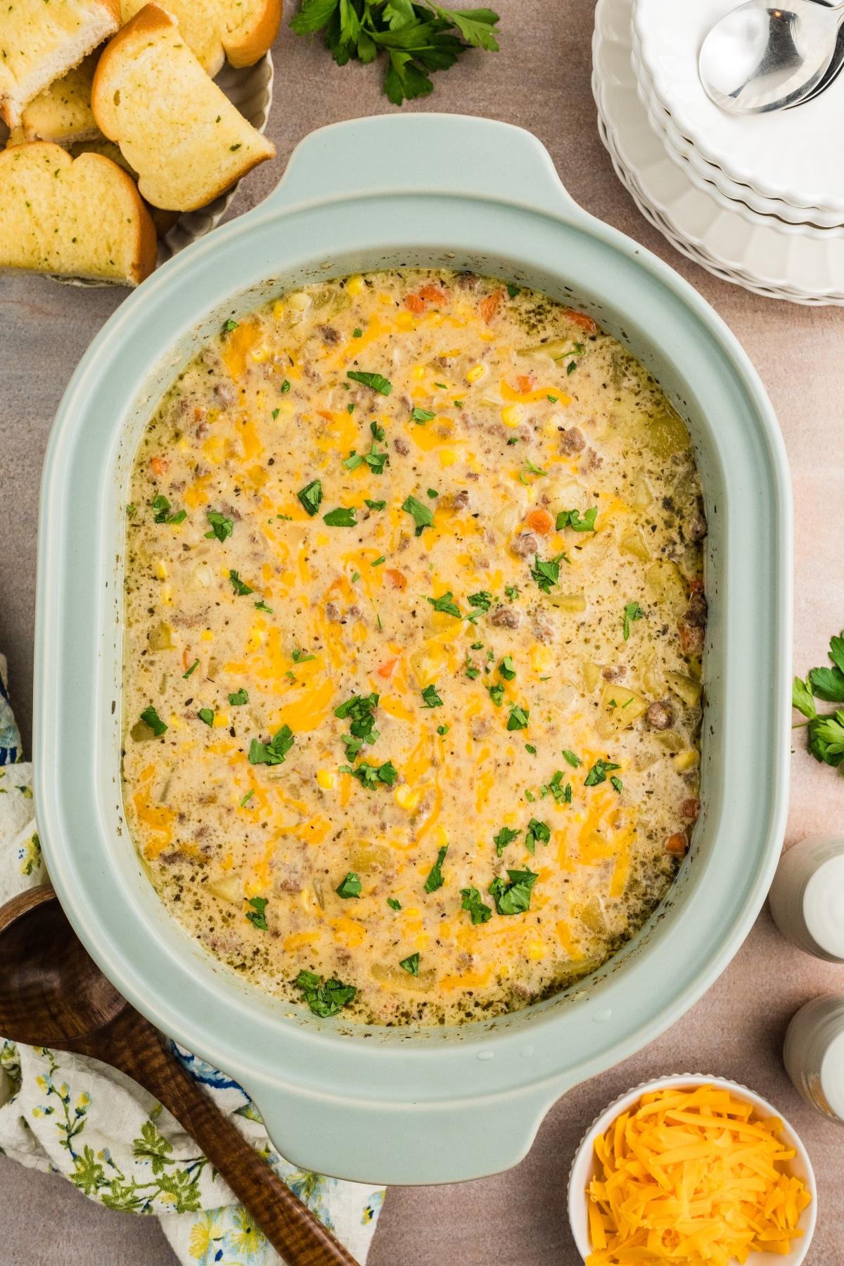 Cheesy soup with ground meat and herbs in a casserole dish, surrounded by bread slices and bowls.