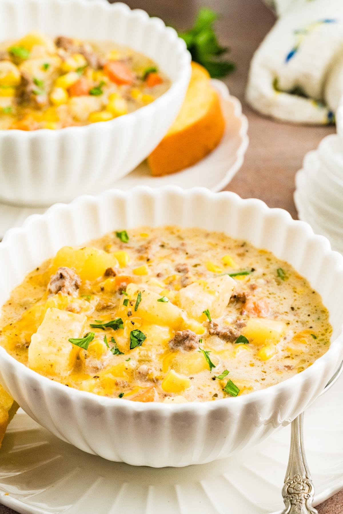 Two bowls of slow cooker cheeseburger creamy soup with ground meat, potatoes, corn, and herbs, served with bread on the side.