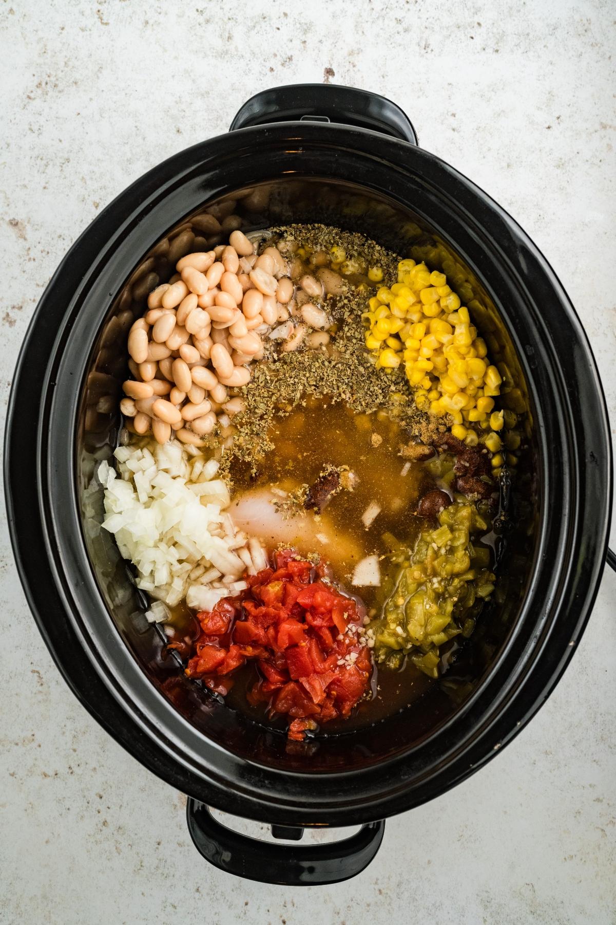 Overhead view of a slow cooker filled with beans, corn, onions, tomatoes, green chilies, and spices.