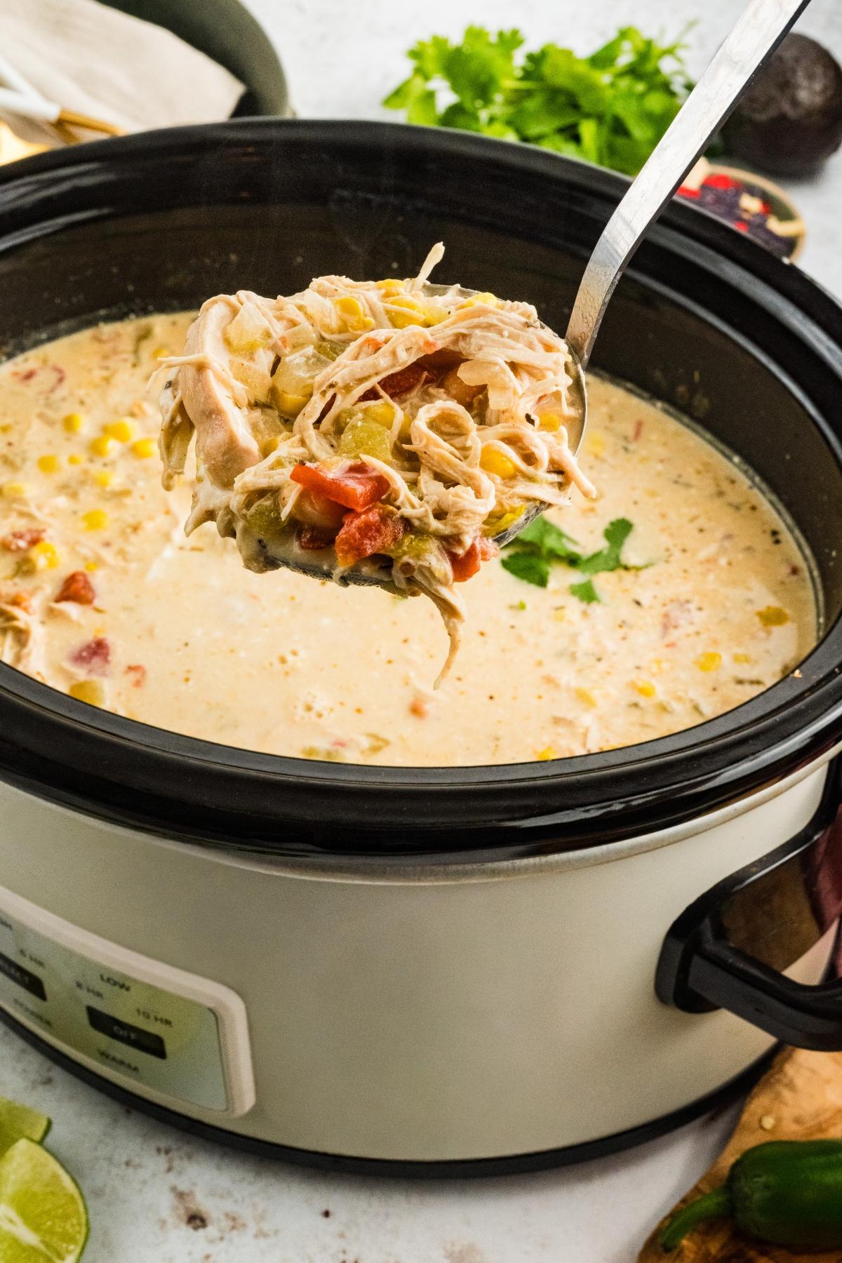 A ladle lifts creamy  slow cooker green chile  chicken soup with vegetables from a slow cooker.