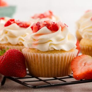 Strawberry Shortcake Cupcakes: Vanilla cupcakes with whipped cream frosting and chopped strawberries, surrounded by fresh strawberries.