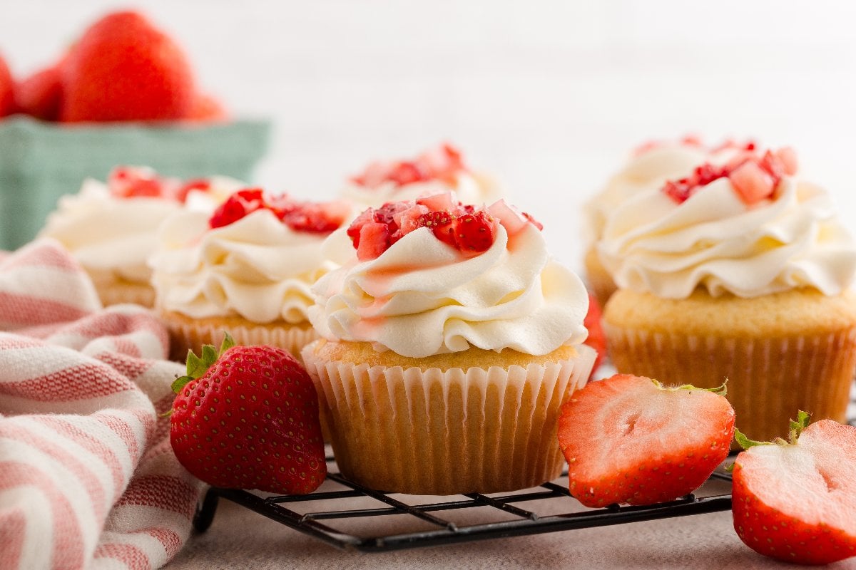 Strawberry Shortcake Cupcakes with vanilla cake, swirled frosting, and chopped strawberries, surrounded by fresh strawberries.