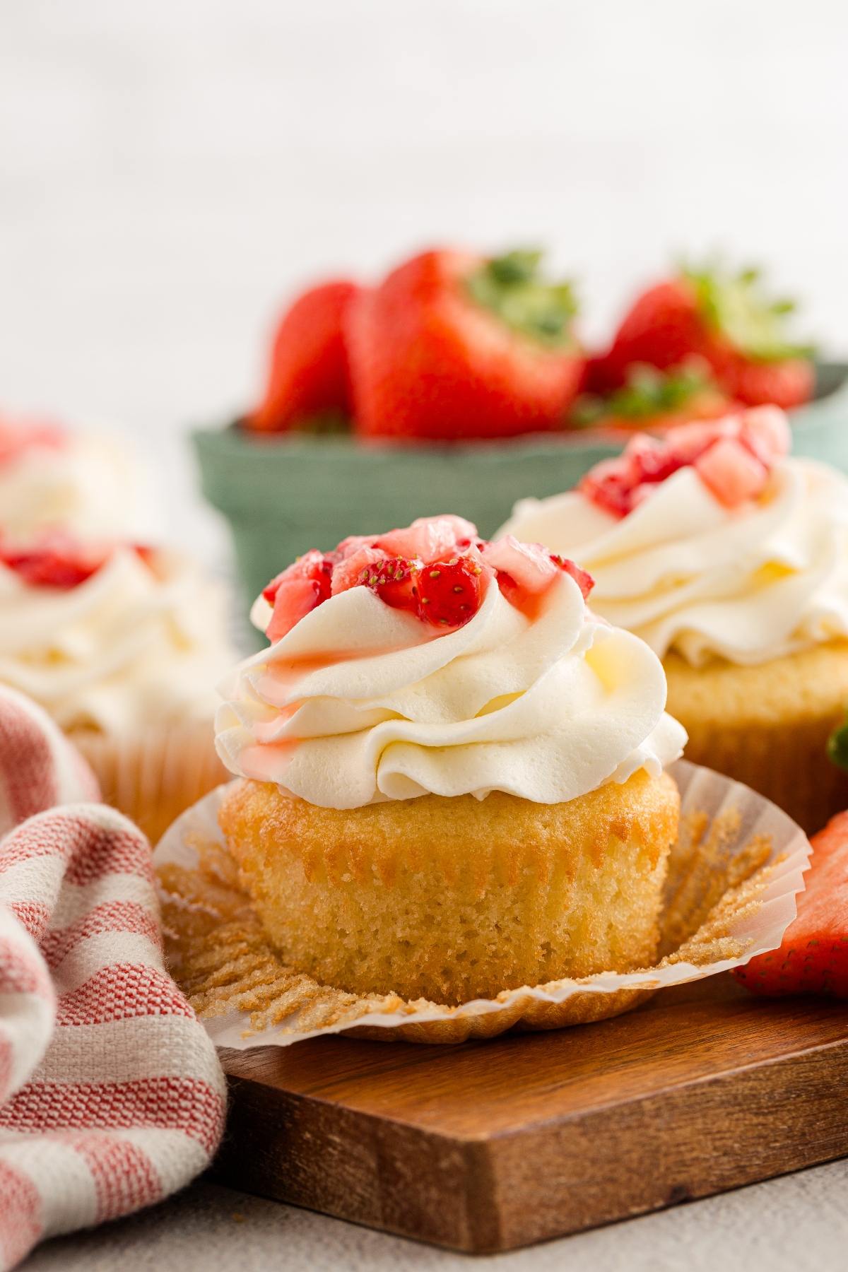 A strawberry shortcake cupcakes with whipped cream and strawberry topping, with fresh strawberries in the background.