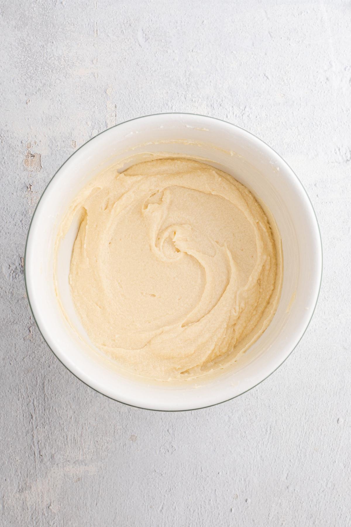 White bowl filled with smooth, creamy cake batter on a light textured surface.