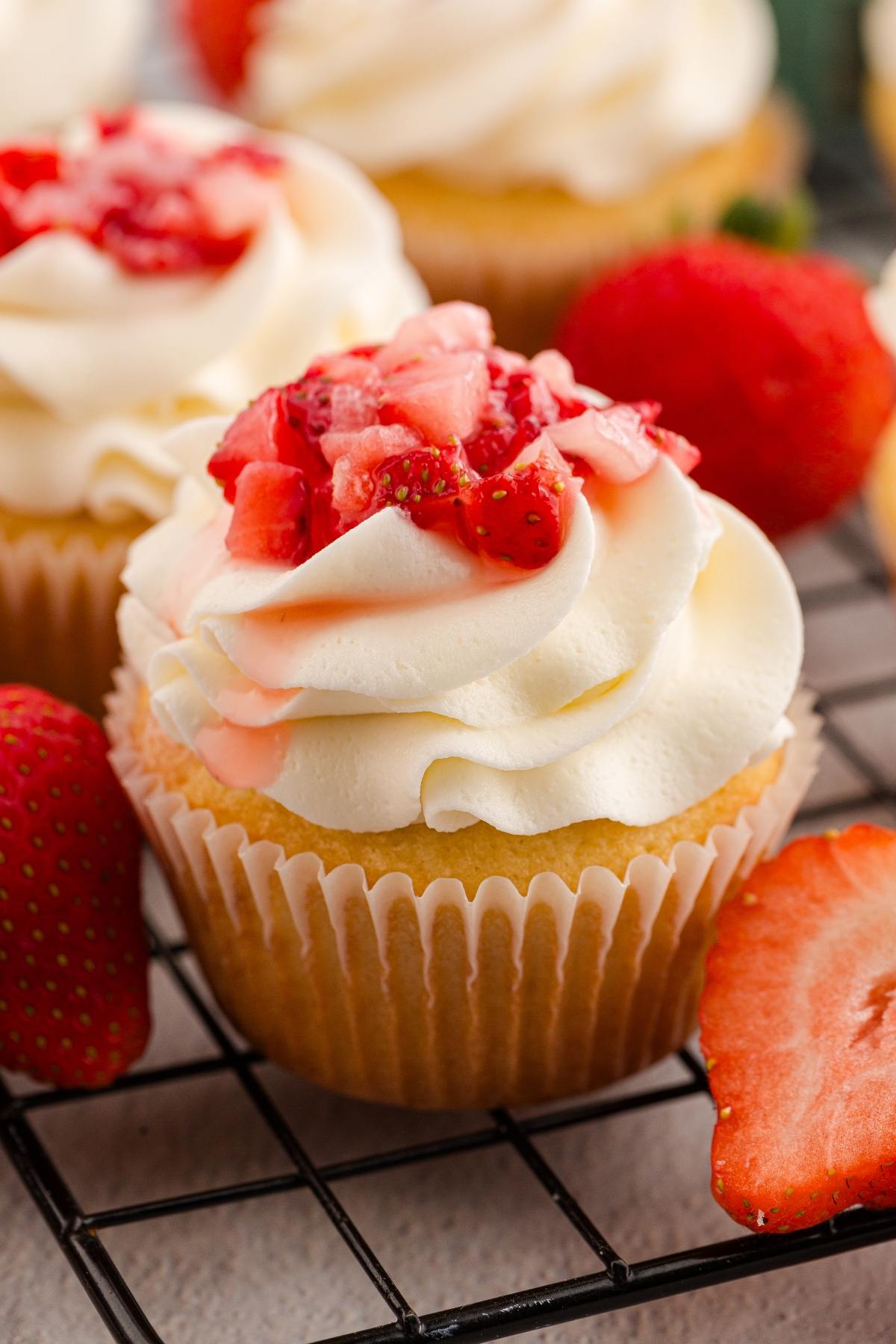 strawberry shortcake cupcakes with whipped frosting and chopped strawberries on top, surrounded by fresh strawberries.