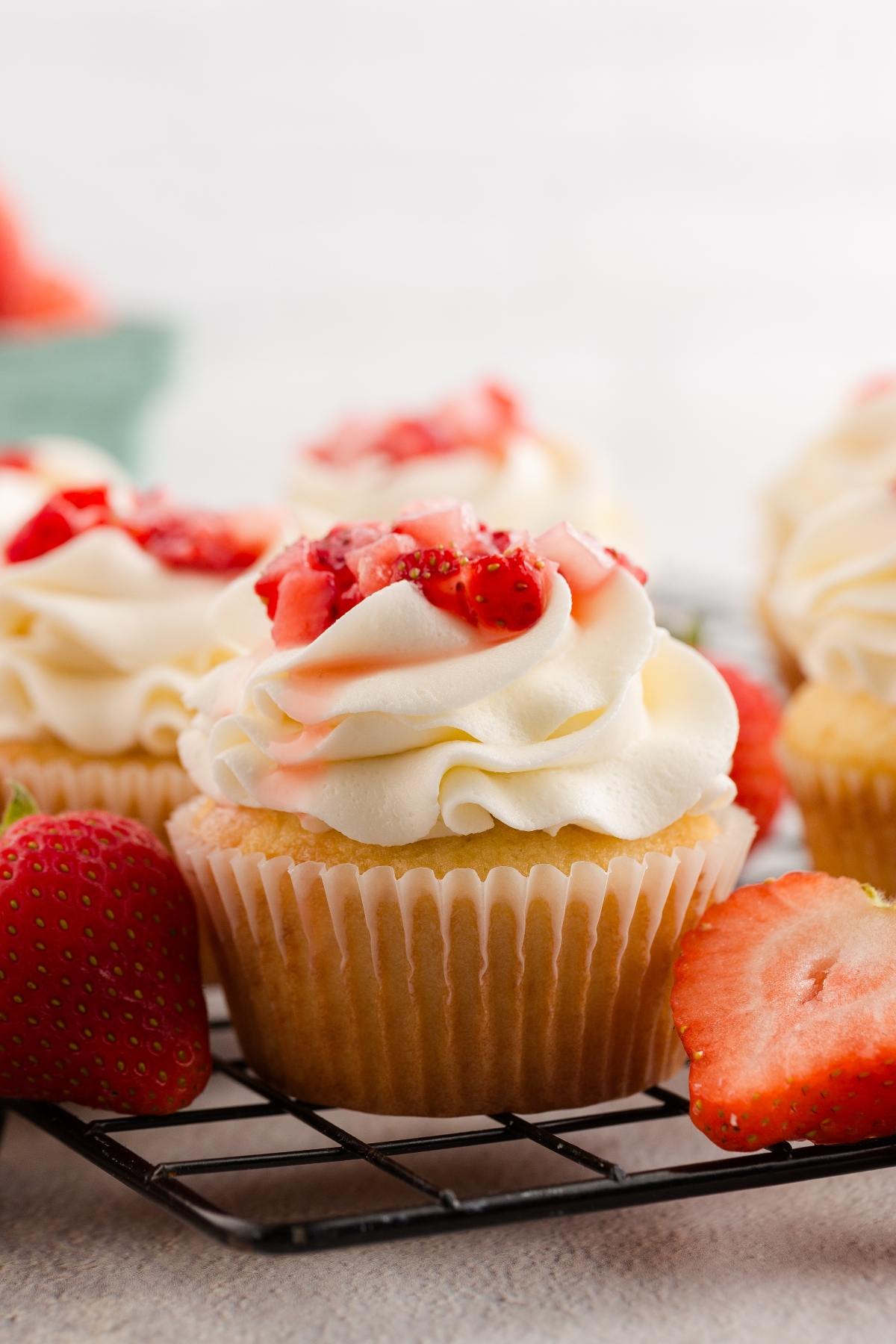 strawberry shortcake cupcakes with swirled frosting and sliced strawberries on top, surrounded by fresh strawberries.