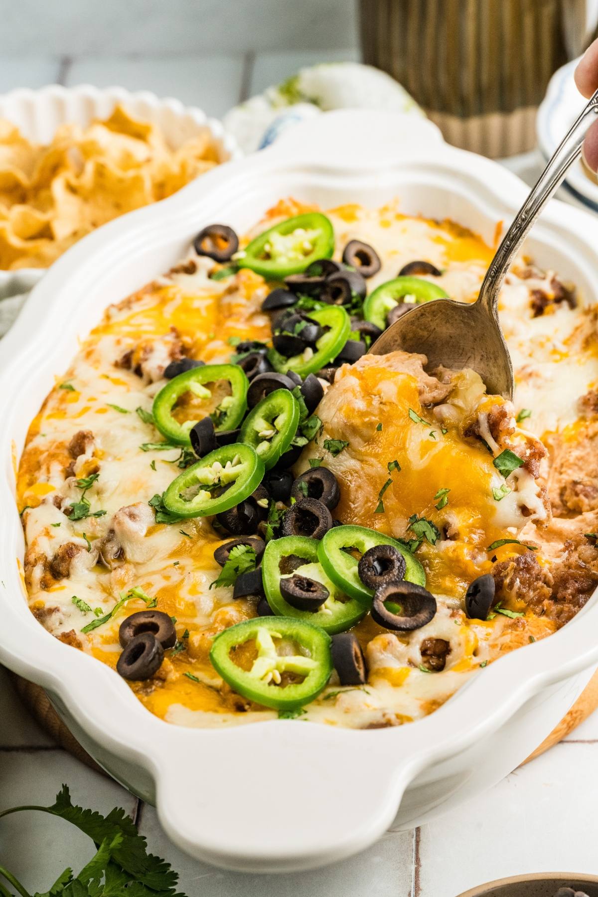 Casserole topped with melted cheese, sliced jalapeños, and black olives, served with a spoon.