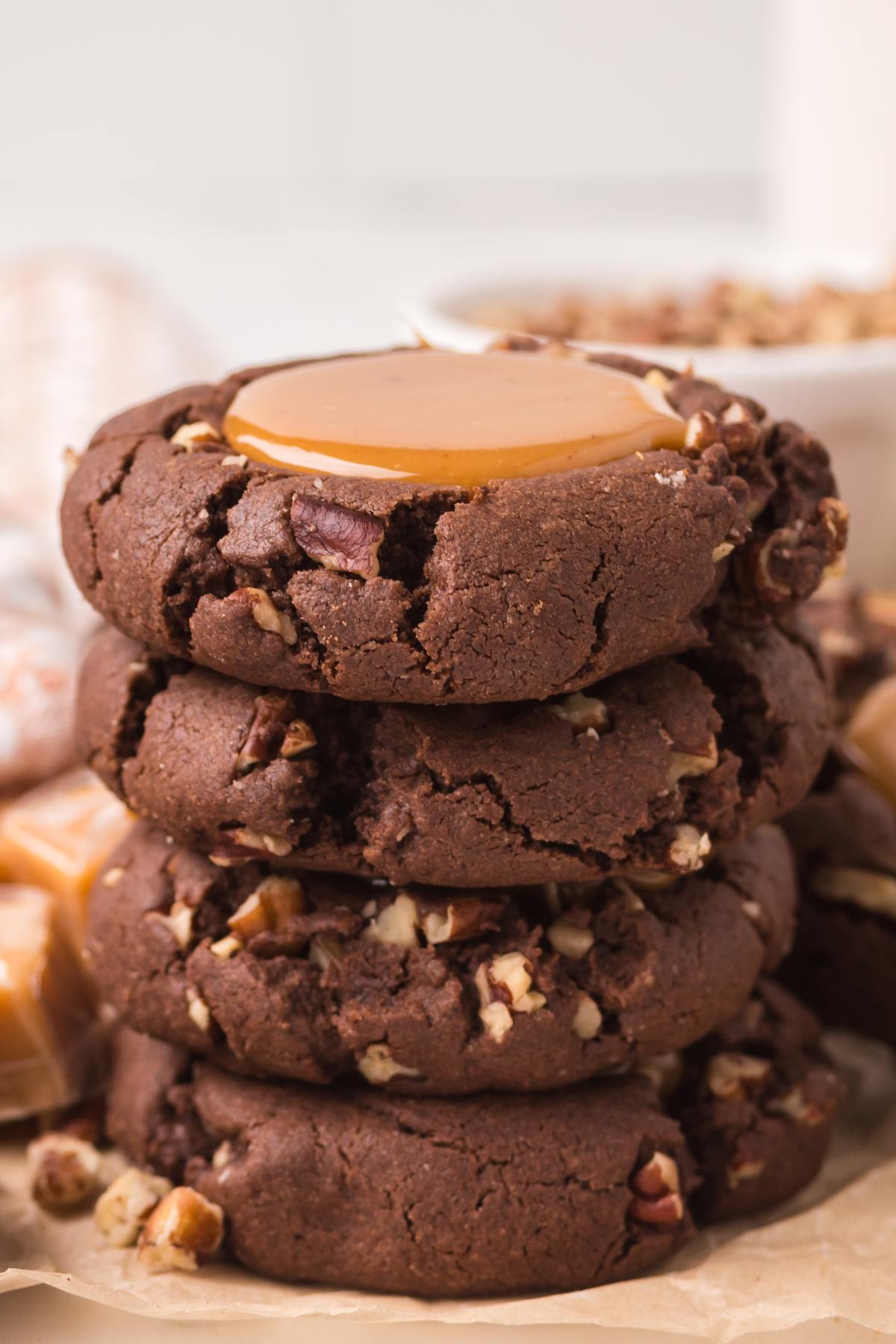 A stack of chocolate turtle cookies with pecans and caramel centers on parchment paper.