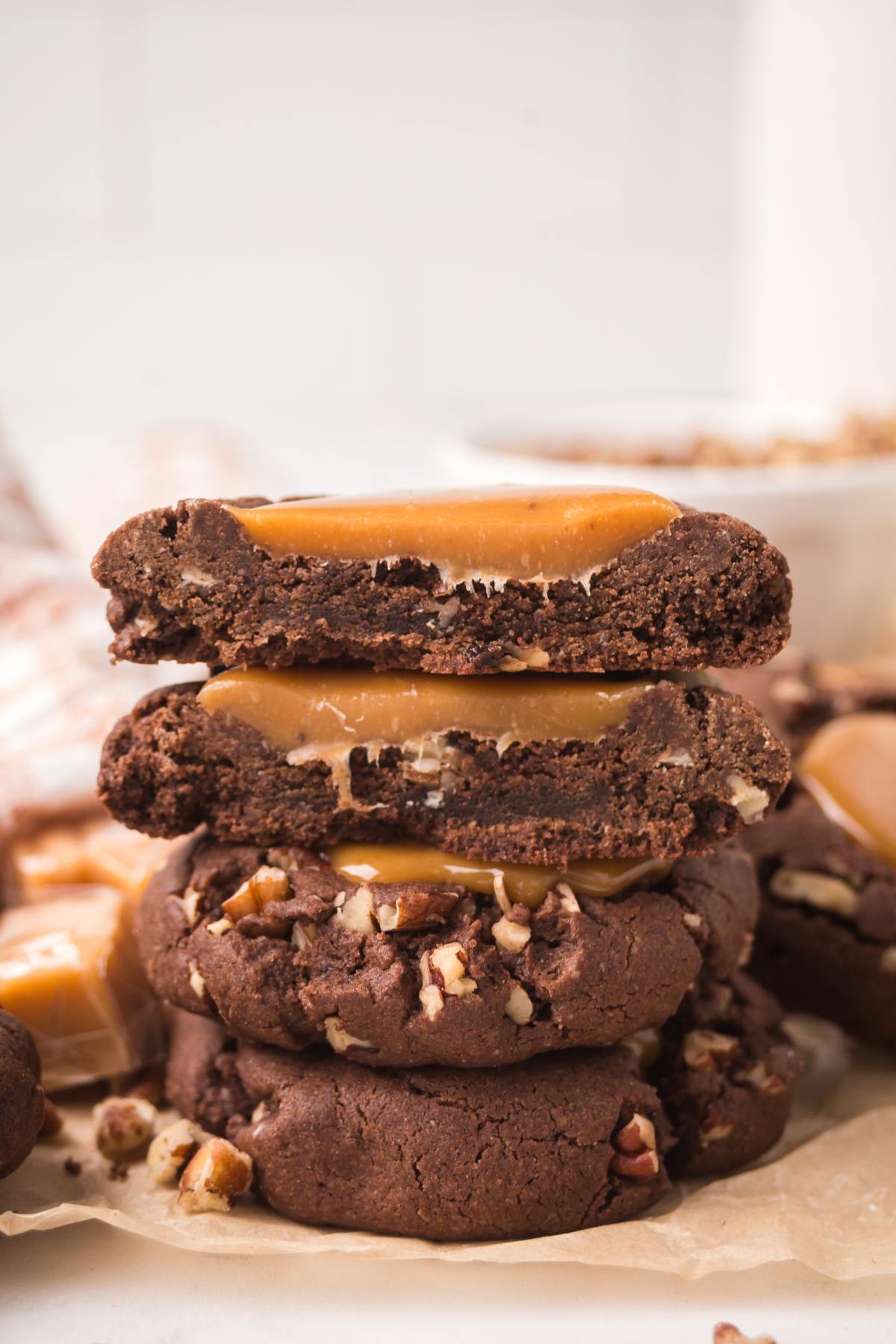 A stack of turtle cookies with caramel and pecans, one cookie broken in half showing the inside.