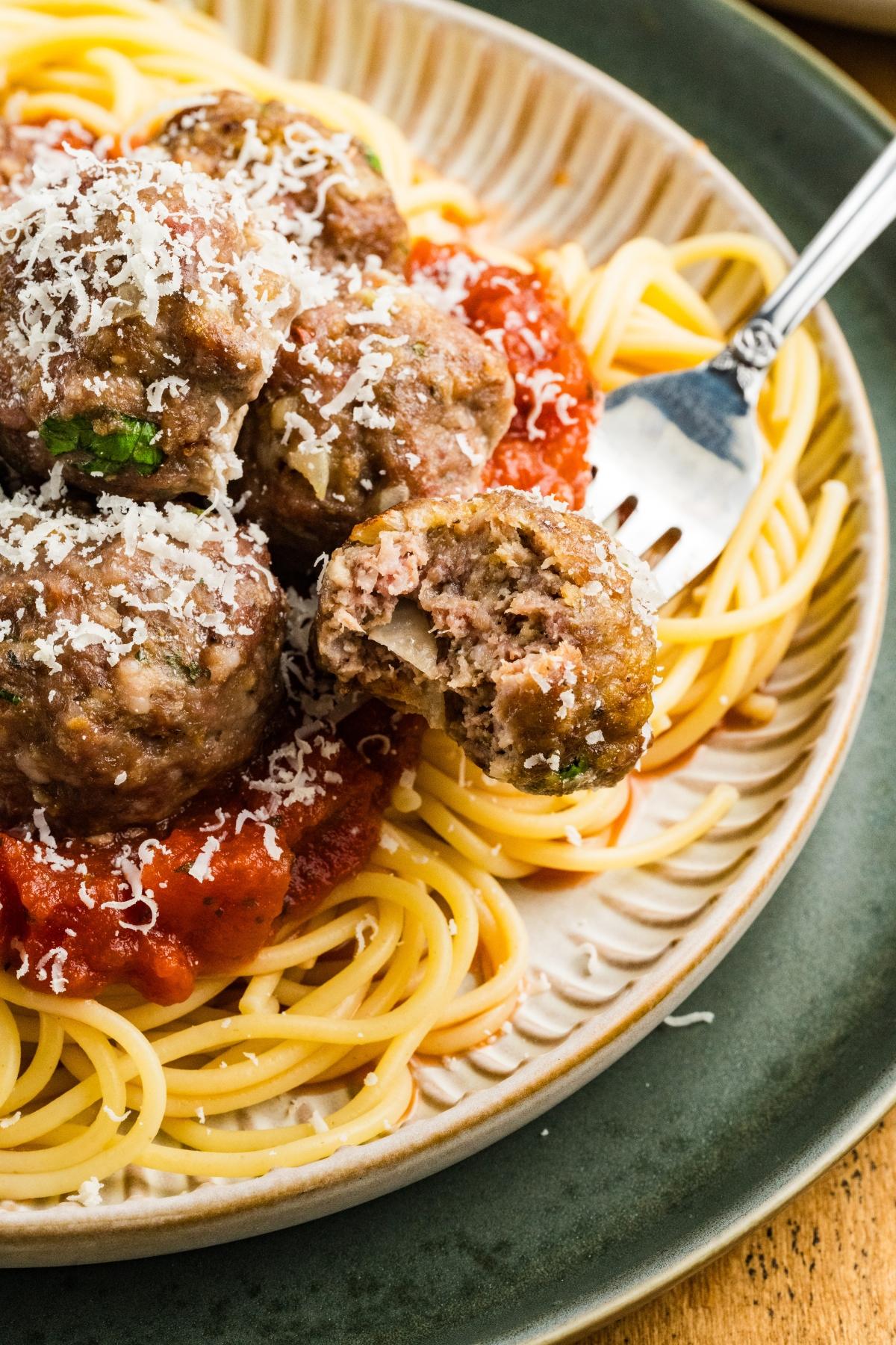 Spaghetti topped with tomato sauce, meatballs, and grated cheese, with a fork holding a bitten meatball.