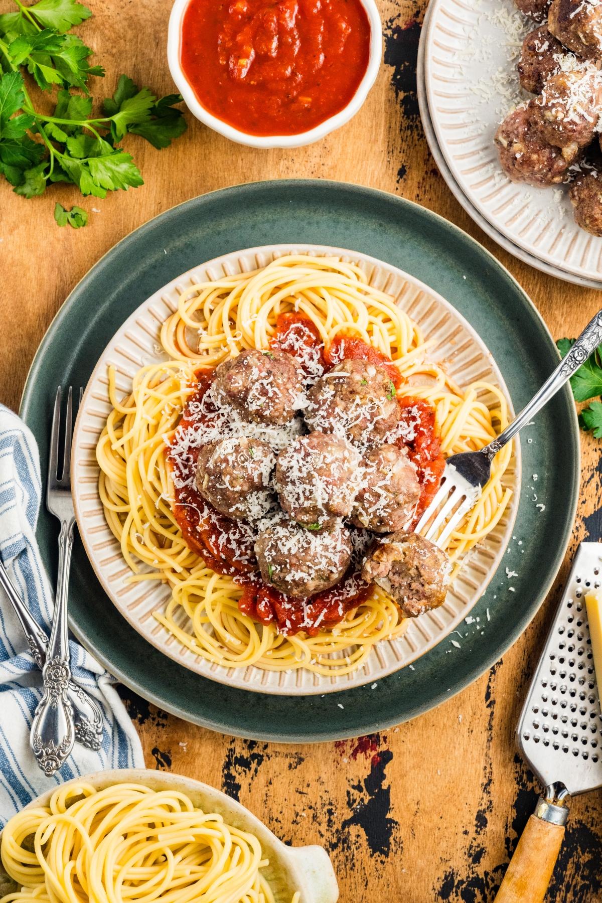 A plate of spaghetti with meatballs, marinara sauce, and grated cheese, served with a fork on a wooden table.