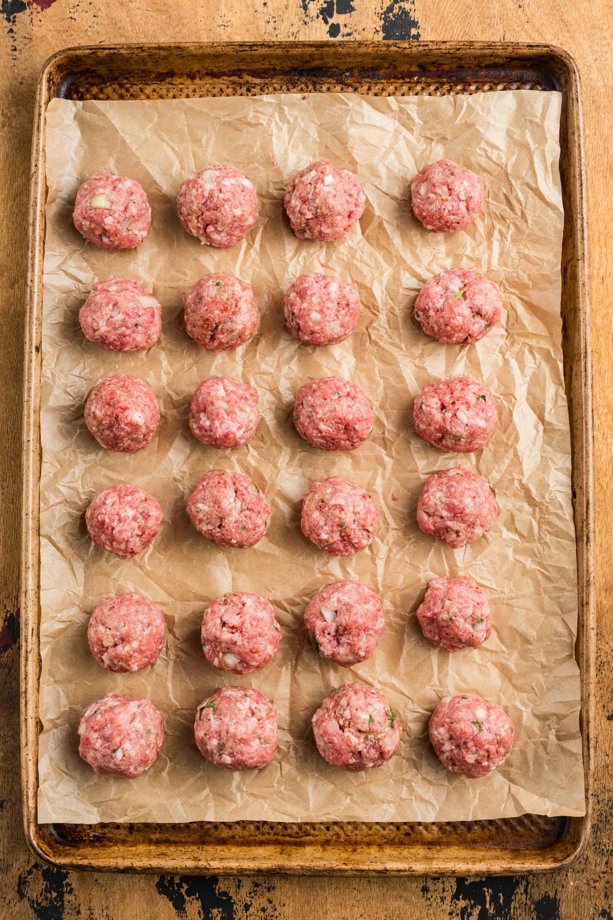 Raw meatballs arranged in rows on a parchment-lined baking sheet, ready to be cooked.