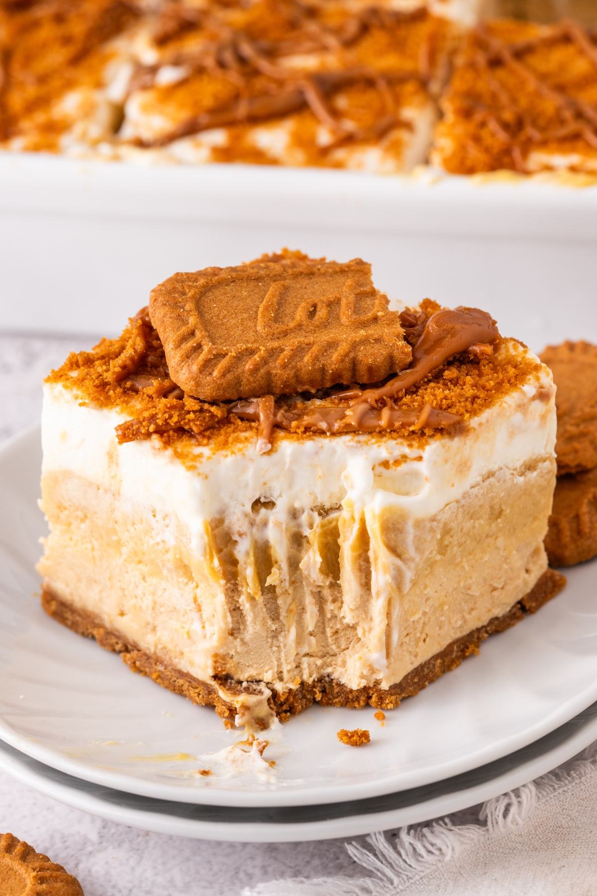 A creamy layered biscoff lush dessert topped with a cookie and crumbs on a white plate, with a bite taken out.