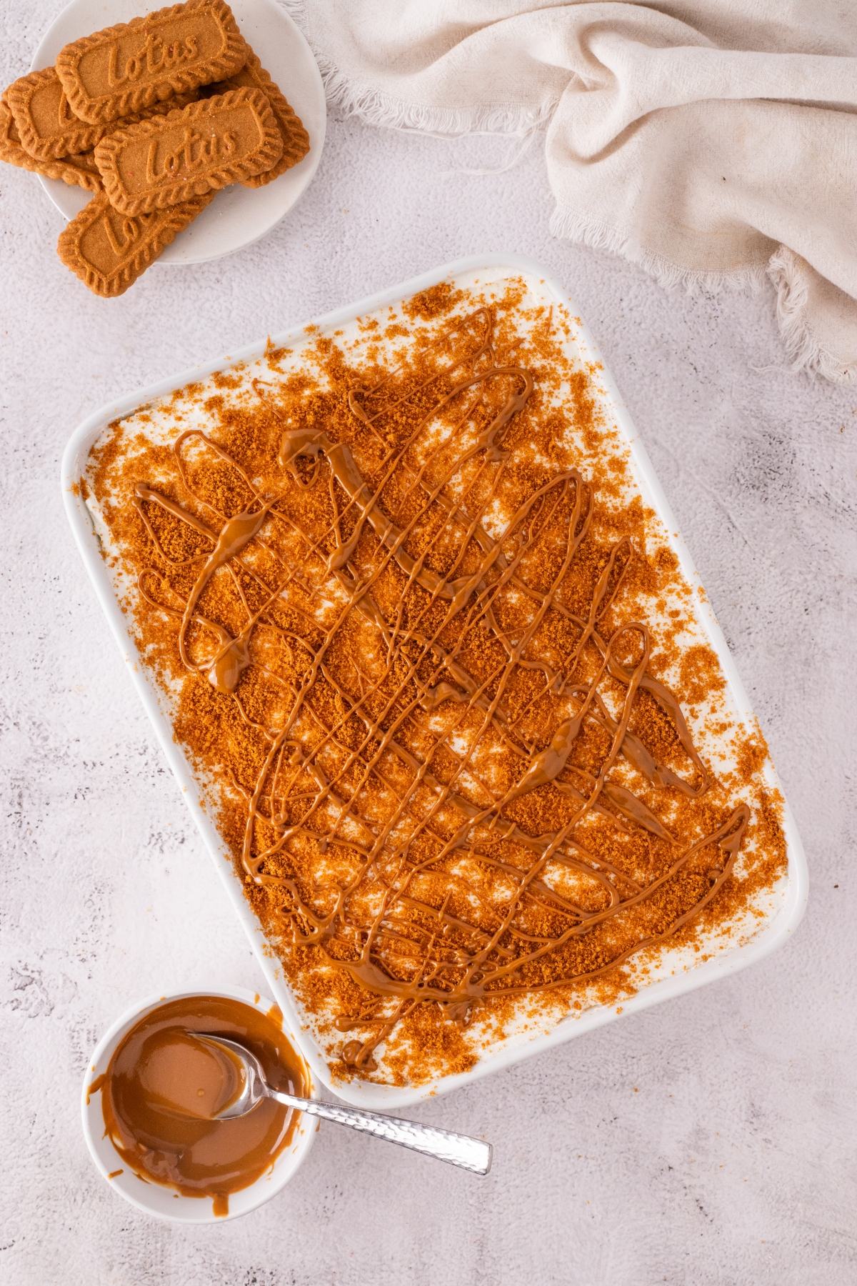 Tray of Biscoff dessert topped with cookie crumbs and drizzle, with cookies and melted spread on the side.