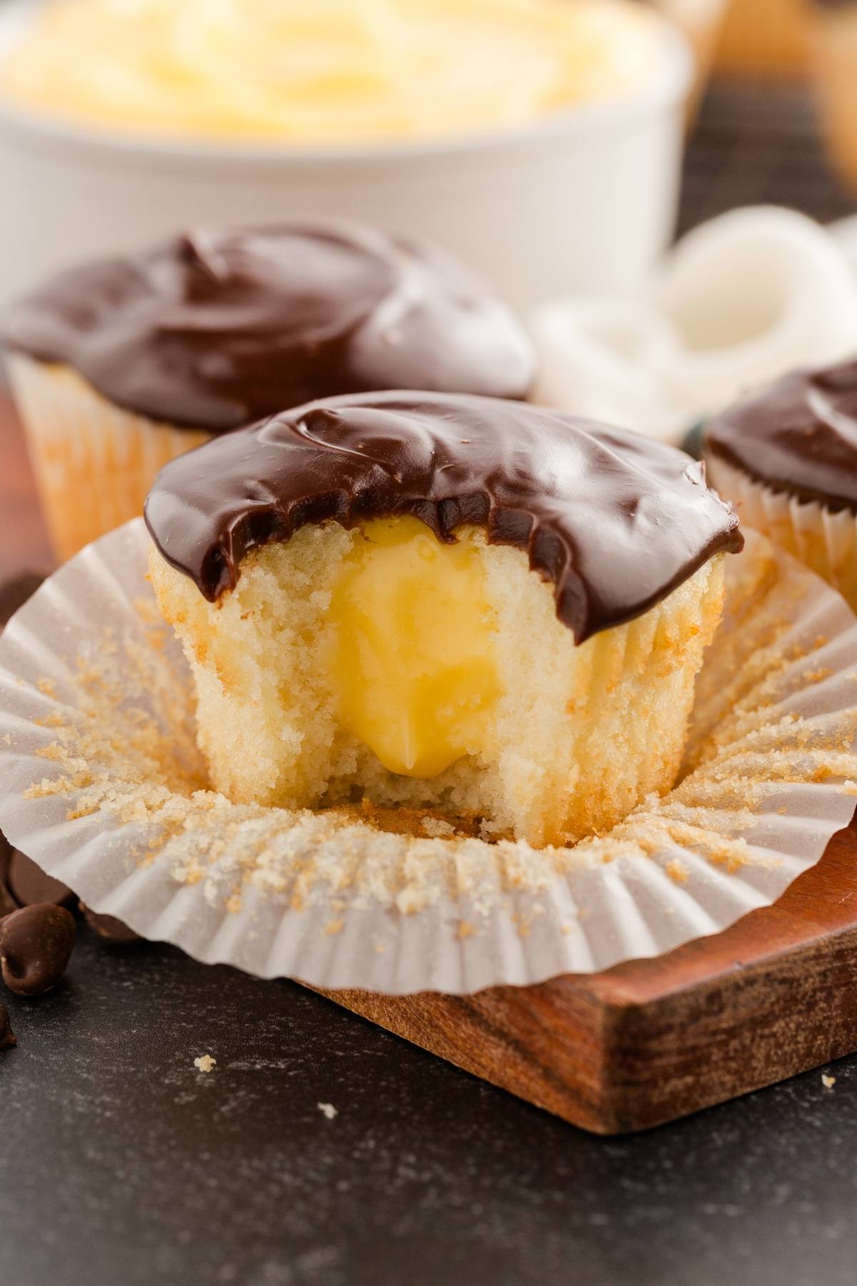 Vanilla boston cream cupcake with chocolate frosting and a creamy yellow filling, with a bite taken out.