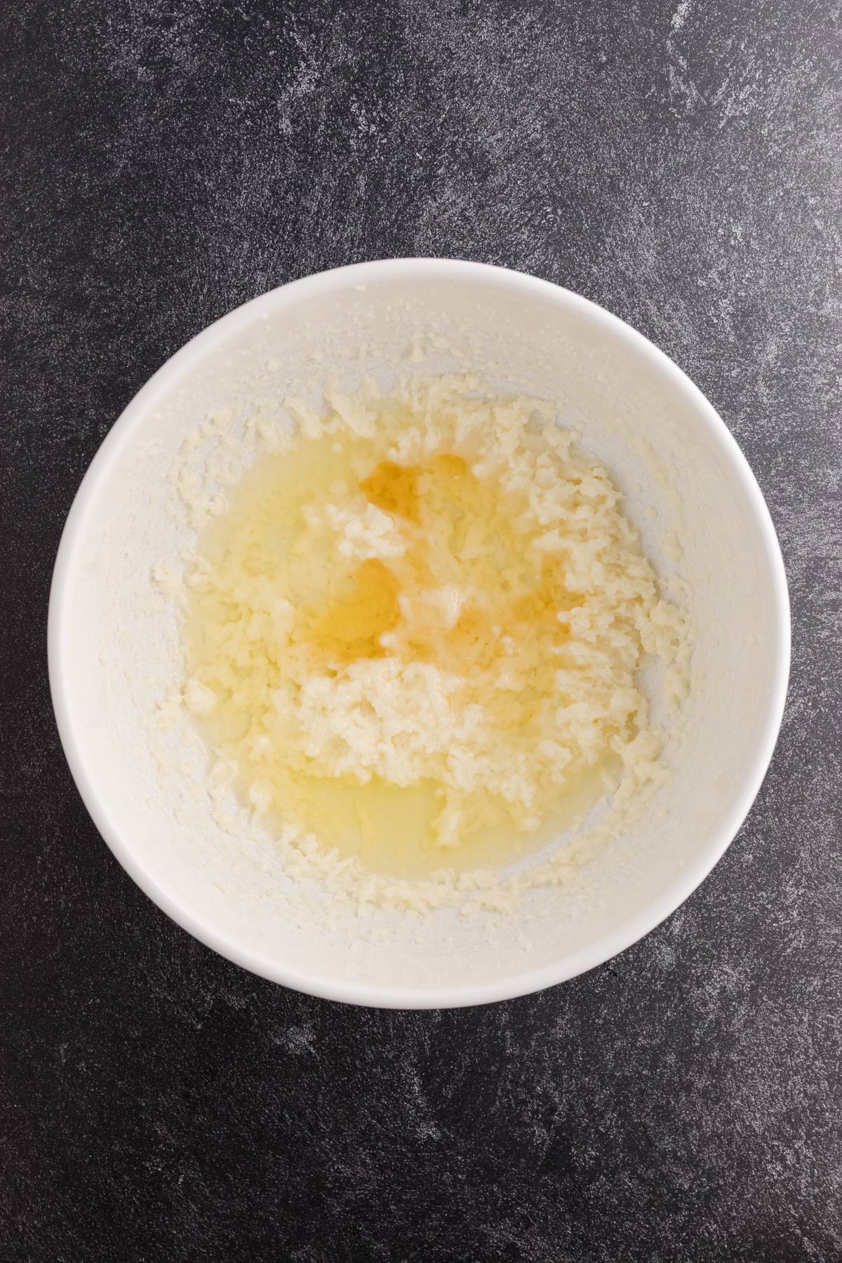A white bowl with creamed butter and sugar, topped with eggs, on a dark countertop.